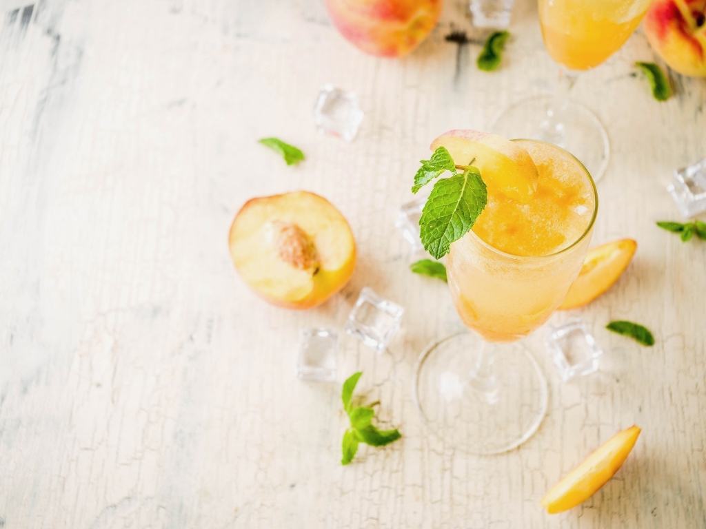 peach bellini glass surrounded by peaches