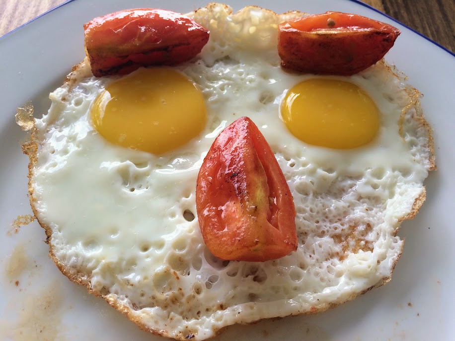 Three fried eggs with tomatoes that make a face