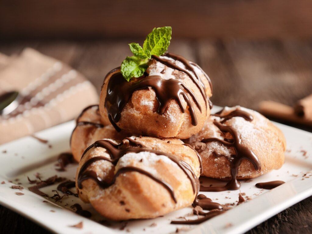 Pile of profiteroles with chocolate sauce and mint garnish