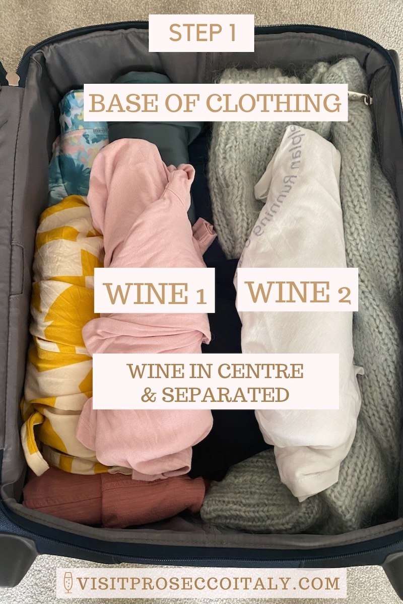 Suitcase showing base of clothing with wrapped wine on top.